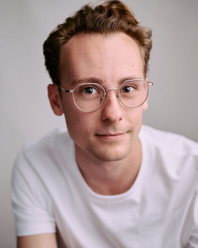 "Morgan in headshot photography, wearing a white T-shirt and wire-rimmed glasses in the Brighton studio.