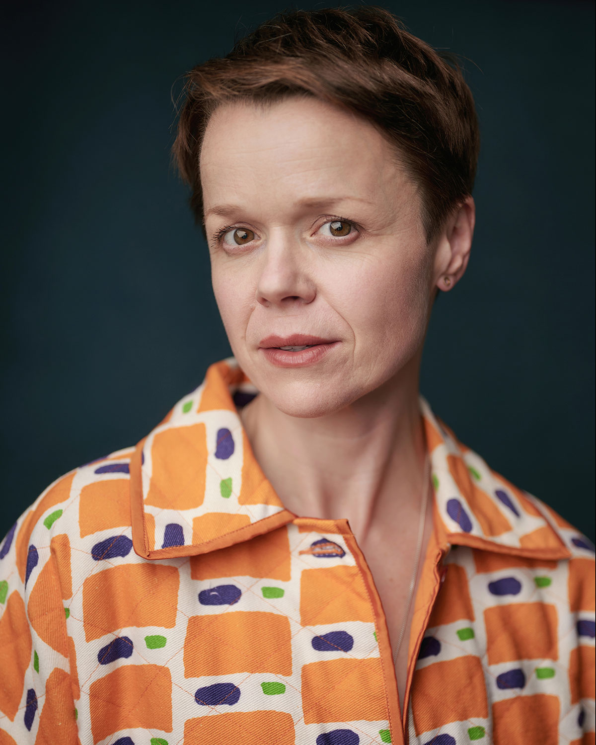 Hannah Barrie in headshot photography, wearing an orange and white shirt against a grey background
