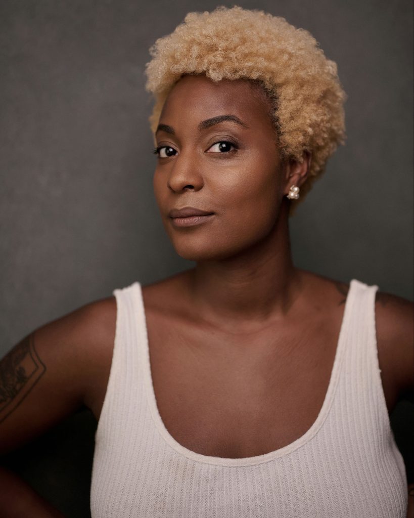 Syd Sainte in headshot photography, wearing a white vest against a grey background.