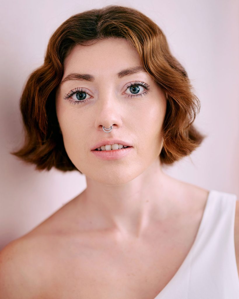 Gabriella Leonardi in headshot photography, wearing a white shirt against a pink background.